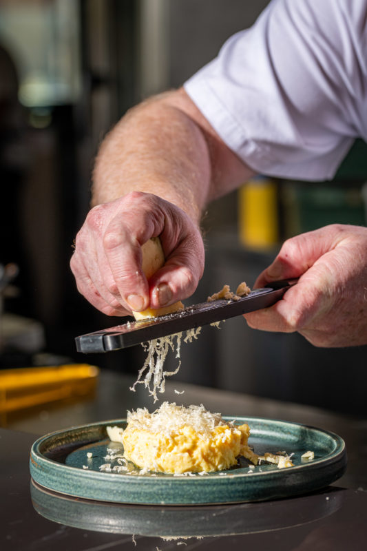 Server is scraping cheese onto a plate